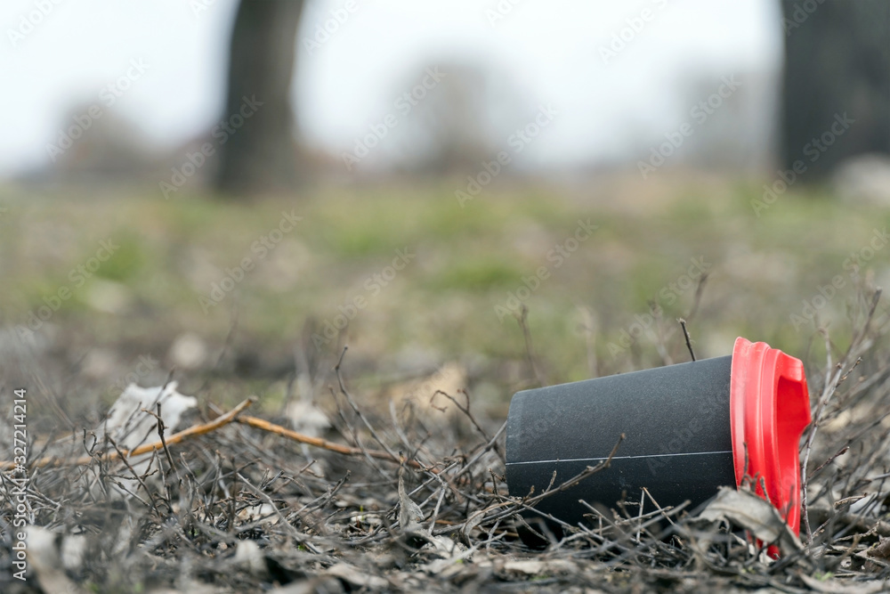 Enviromental pollution; paper cup for coffee and red plastic cover on a background of forest nature and grass. Black coffee cup rubbish in grass, close up, copyspace for text on picture. Enviromental pollution; paper cup for coffee and red plastic cover on a background of forest nature and grass. Black coffee cup rubbish in grass, close up, copyspace for text on picture.