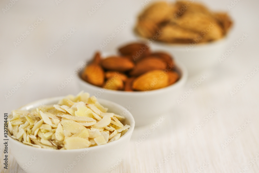 Coconut flakes and almonds in three white bowls on a white surface Coconut flakes and almonds in three white bowls on a white surface