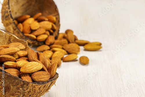 Two half coconut shell with almonds on a white background