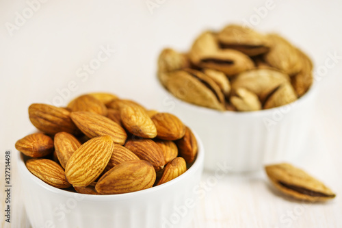 Two white bowls with peeled and unpeeled almonds on a white surface