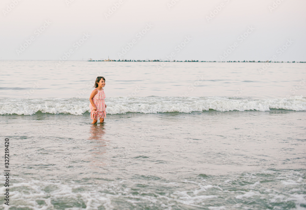 Little girl with pink dress having fun in sea water