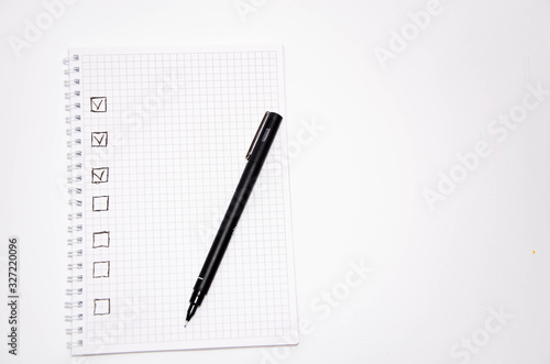 Check list. Square items are empty and checked with a tick. Squared notebook with black pen on a white background. Record ideas, notes, plans, tasks.  Copy Space