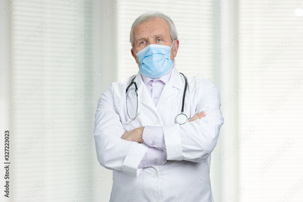 Serious doctor with medical mask and crossed arms. Portrait of senior experienced physician in protective mask and stethoscope. Serious doctor with medical mask and crossed arms. Portrait of senior experienced physician in protective mask and stethoscope.