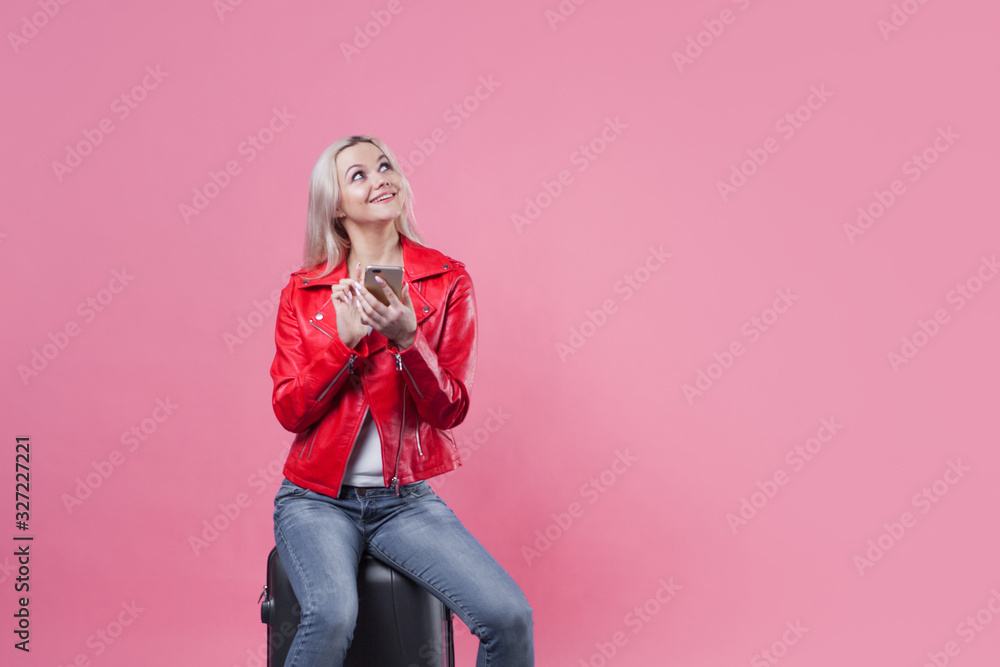 young female tourist in a jacket and with Luggage on a pink background. young female tourist in a jacket and with Luggage on a pink background.