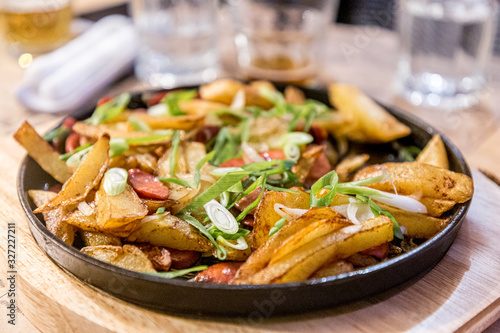 Fried potatoes with sausage on a black cast-iron pan in a restaurant.