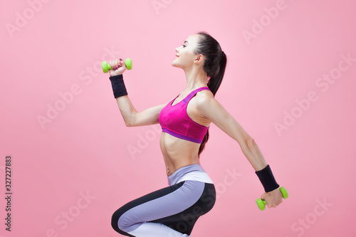 Young athletic brunette girl in a bright sports top and with a ponytail, runs with green dumbbells and hair fluttering.