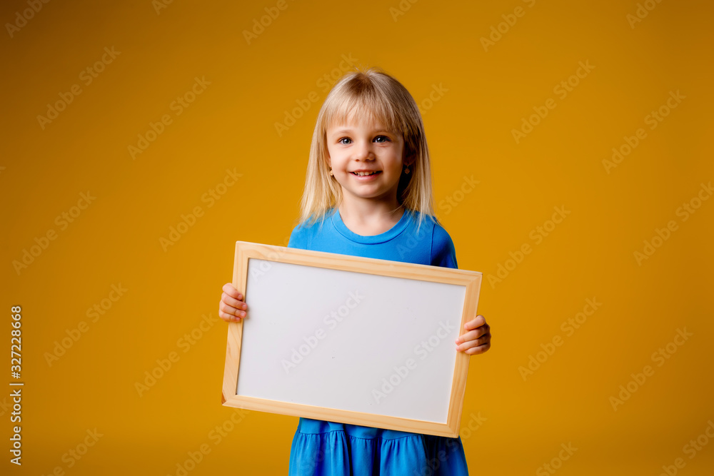little blonde girl in a blue dress and a striped hat holds a white record board on a yellow background little blonde girl in a blue dress and a striped hat holds a white record board on a yellow background