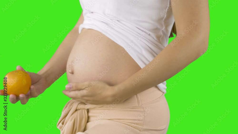 A happy pregnant young woman holding an orange next to her belly