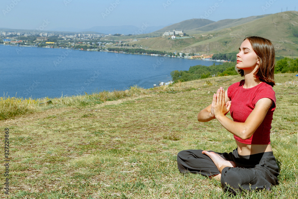 Concentrated woman doing yoga in lotus pose in mountain area. Side view of relaxed and contented female with closed eyes sitting in asana on grass and breathing fresh air 