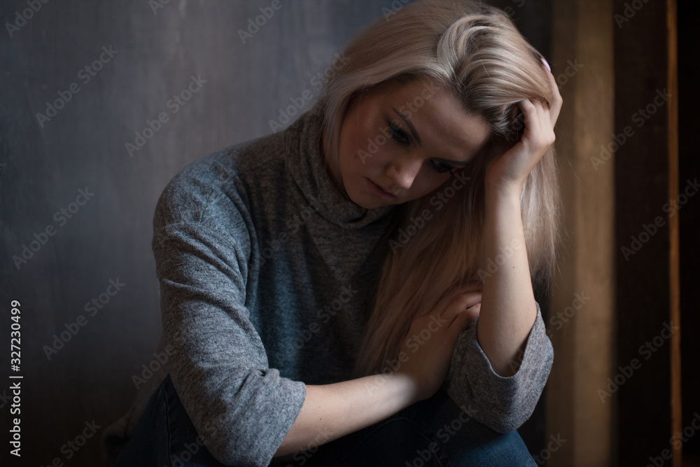 Sad woman sits on the floor. Depression and chronic fatigue. Young beautiful blonde in a gray sweater and jeans Sad woman sits on the floor. Depression and chronic fatigue. Young beautiful blonde in a gray sweater and jeans