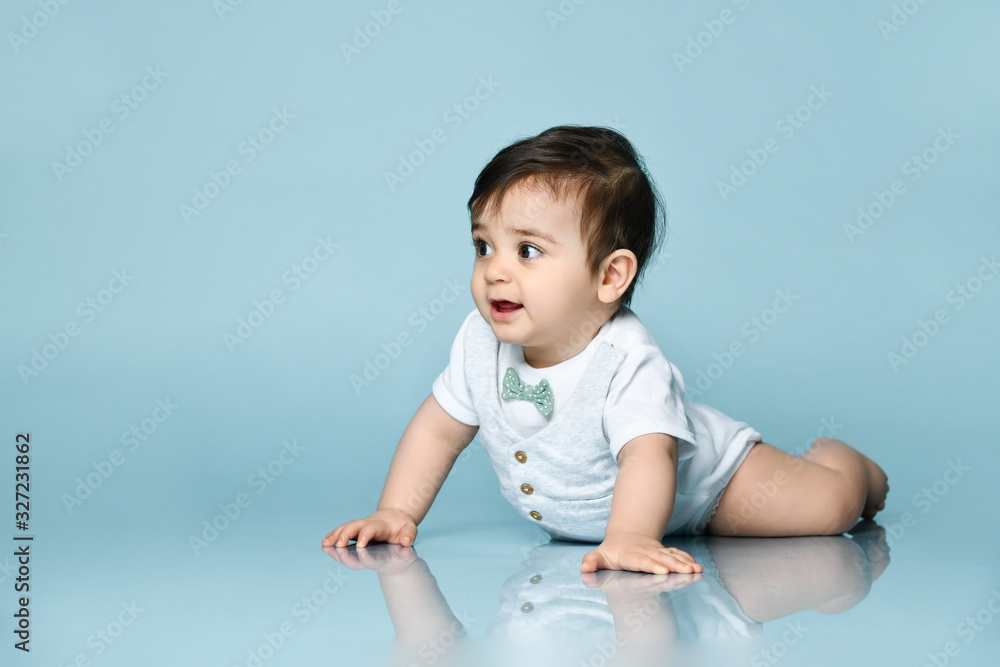 Baby boy in white bodysuit as a vest with bow-tie, barefoot. He is laying on the floor against blue background. Close up Baby boy in white bodysuit as a vest with bow-tie, barefoot. He is laying on the floor against blue background. Close up