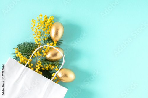 Easter composition with mimosa flowers. Branches flowers mimosa, Easter golden eggs on bright blue background. Flat lay, top view, copy space