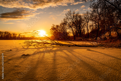 Beautiful wide angle view of the fallen tree on the shore of a frozen river at sunset. Travel destination Russia