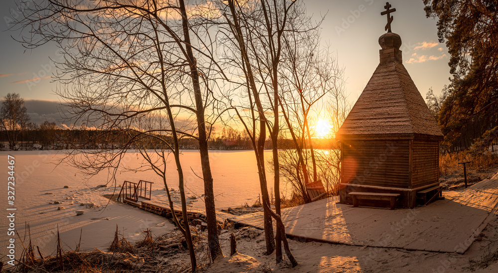 Beautiful wide angle view of old wooden bathhouse on the shore of a frozen river at sunset. Travel destination Russia