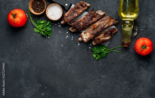 Grilled pork ribs over meat knife with spices on a stone background with copy space for your text.