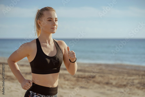 woman running seaside with sport clothers and smart watches on hand; female jogger waist-high view training; sport and fitness concept.