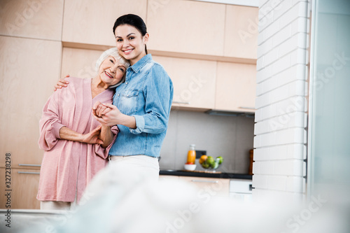 Smiling young lady hugging grandmother and holding her hand