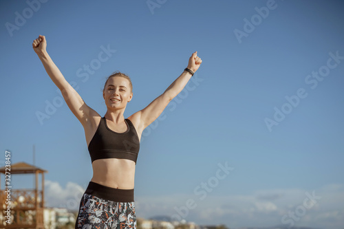 happy woman raise hands up  female with sportwear on blue sky background: fitness and motivation concept. © valeriyakozoriz