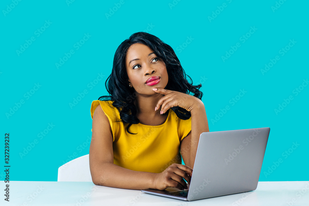 Portrait of a young woman sitting behind desk and computer laptop, looking up thinking Portrait of a young woman sitting behind desk and computer laptop, looking up thinking