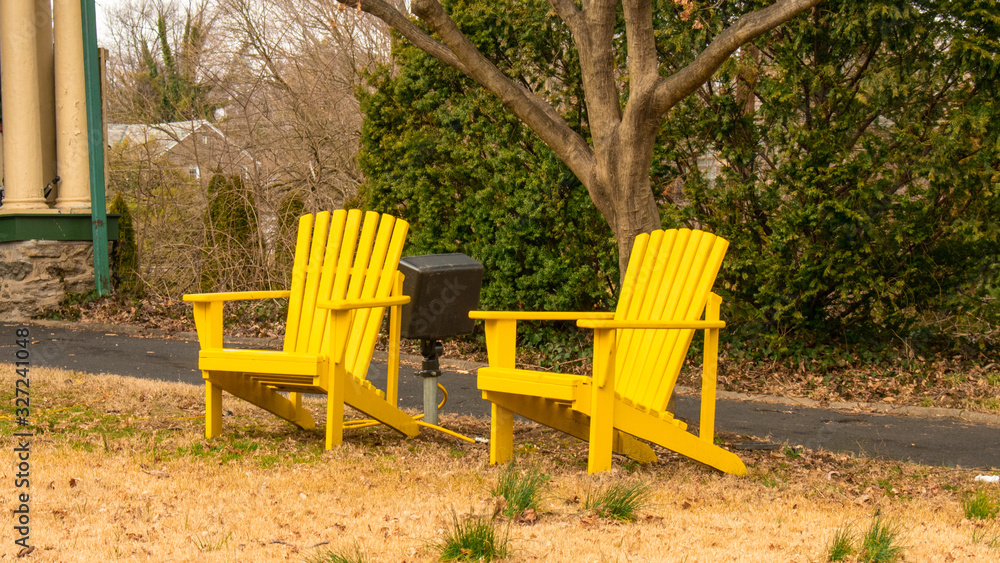 Two Bright Yellow Wooden Lawn Chairs on a Dead Lawn With a Driveway in the Background Two Bright Yellow Wooden Lawn Chairs on a Dead Lawn With a Driveway in the Background
