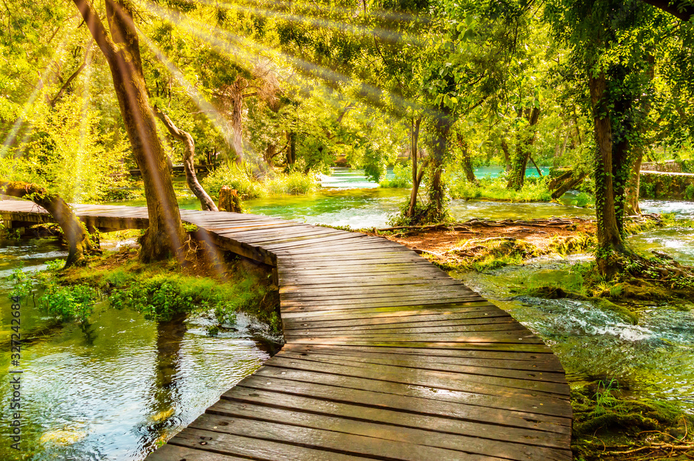 Wooden footpath over river in forest of Krka National Park, Croatia. Beautiful scene with trees, water and sunrays. Wooden footpath over river in forest of Krka National Park, Croatia. Beautiful scene with trees, water and sunrays.