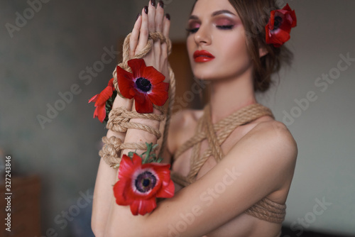 A beautiful girl for the Japanese traditional technique of knitting shibari and flowers. Tender photo shoot at home.