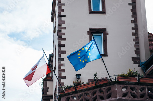 Waving Flag with the coat of arms of Poland and European Union flags waving above the entrance of general consulate or embassy building