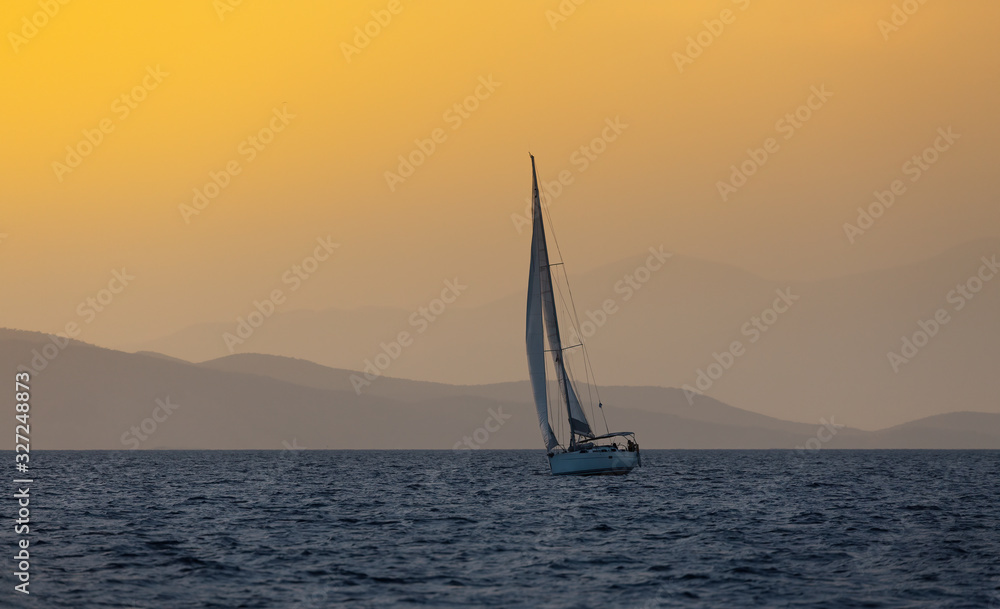Sail boat in open sea at golden hour in evening. Mountains Silhouette in background. Summer adventure, active vacation in Mediterranean sea
