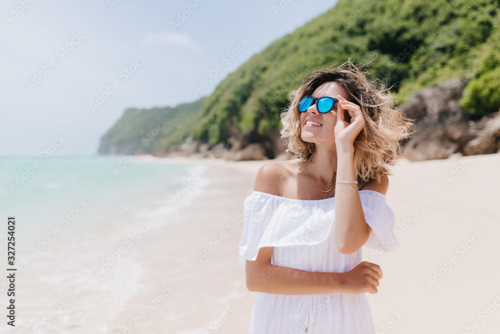 Enthusiastic european woman in summer outfit looking at sky. Outdoor portrait of smiling pretty lady posing during rest at beach.