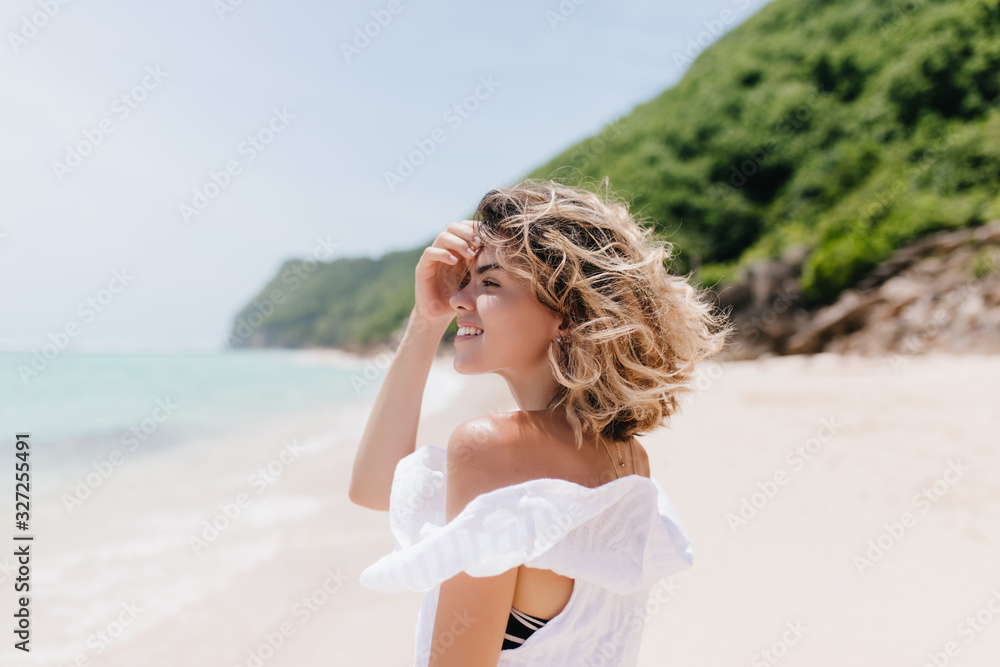 Refined young woman with short light hair looking at sea. Outdoor portrait of lovely tanned girl walking around beach. Refined young woman with short light hair looking at sea. Outdoor portrait of lovely tanned girl walking around beach.