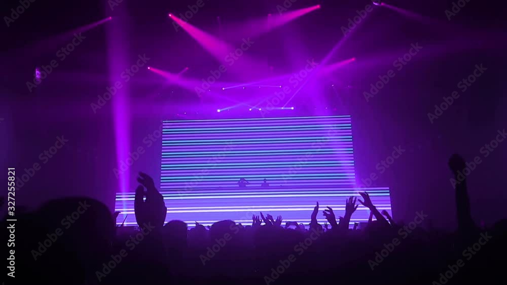 Happy people dance in nightclub party concert and listen to music from DJ on the stage in background. Cheerful crowd celebrate Christmas and New Year party 2018. Young people lifestyle and nightlife.