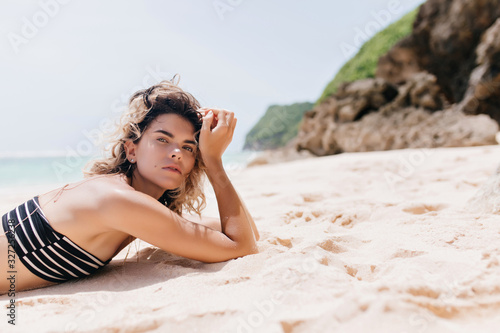 Outdoor portrait of good-humoured lady chilling on nature background. Photo of caucasian jocund girl lying on sandy beach.