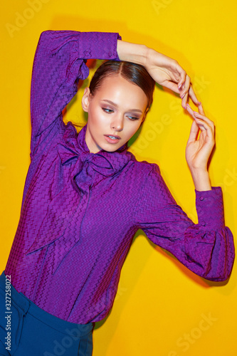 High fashion portrait of young elegant woman. Sudio shot. Violet blouse, blue pants, yellow background © MaxFrost