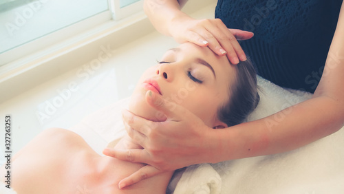 Relaxed woman lying on spa bed for facial and head massage spa treatment by massage therapist in a luxury spa resort. Wellness, stress relief and rejuvenation concept. photo