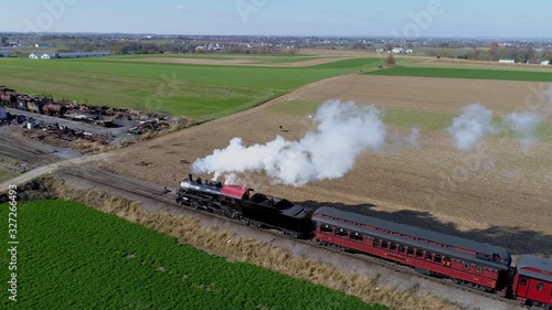 Aerial view of an antique restored steam locomotive with passenger cars pulling into frieght yard as it is  blowing black and white smoke and steam photo