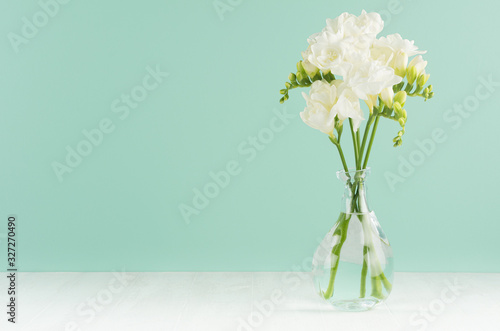 Spring gentle fresh flowers in transparent glass vase in elegant green mint menthe interior on white wood board  copy space.