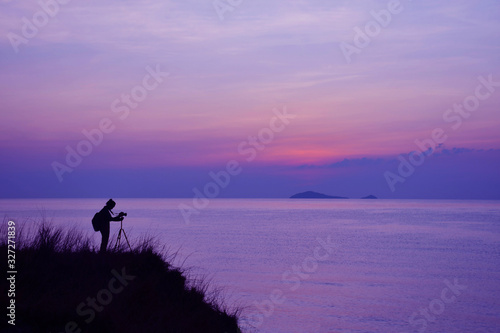 Silhouette of photographer, women standing with a camera on the mountain at sunset blue sky