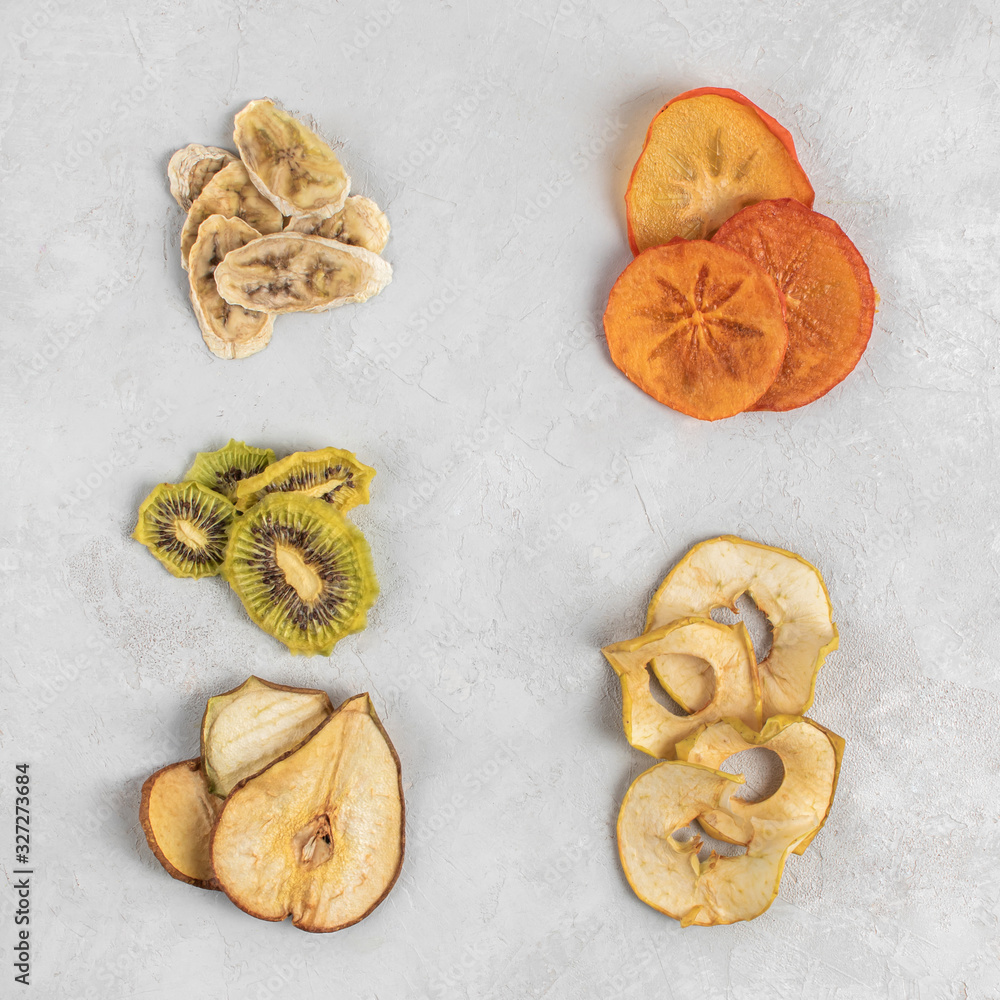 Healthy homemade fruit chips from apple, persimmon, pear, kiwi and banana on grey background. Organic diet food. The vegan diet. Dried fruits. Vegetarian plant based snack concept. Top view. Healthy homemade fruit chips from apple, persimmon, pear, kiwi and banana on grey background. Organic diet food. The vegan diet. Dried fruits. Vegetarian plant based snack concept. Top view.