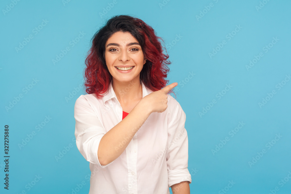 Advertising area, idea presentation. Cheerful hipster woman with fancy red hair in white shirt pointing to side, showing copy space for commercial. indoor studio shot isolated on blue background Advertising area, idea presentation. Cheerful hipster woman with fancy red hair in white shirt pointing to side, showing copy space for commercial. indoor studio shot isolated on blue background