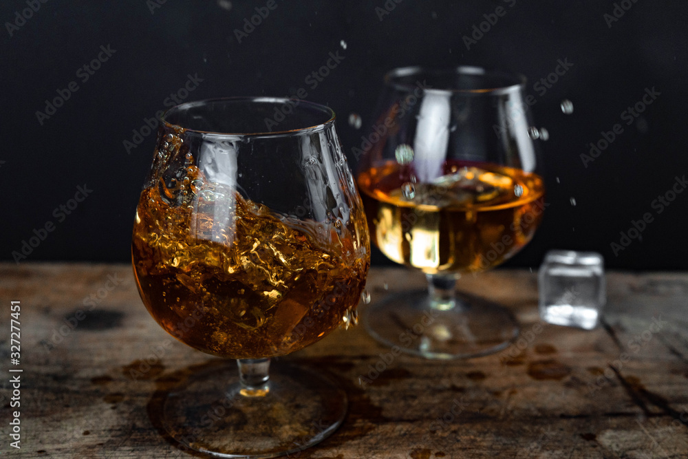 Two whiskey / cognac glasses with ice on a wooden background. Dark backdrop. Two whiskey / cognac glasses with ice on a wooden background. Dark backdrop.