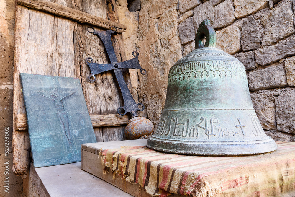 Obraz premium Bell, cross and hammered crucifix on background of masonry and an old wooden shield on handmade rug