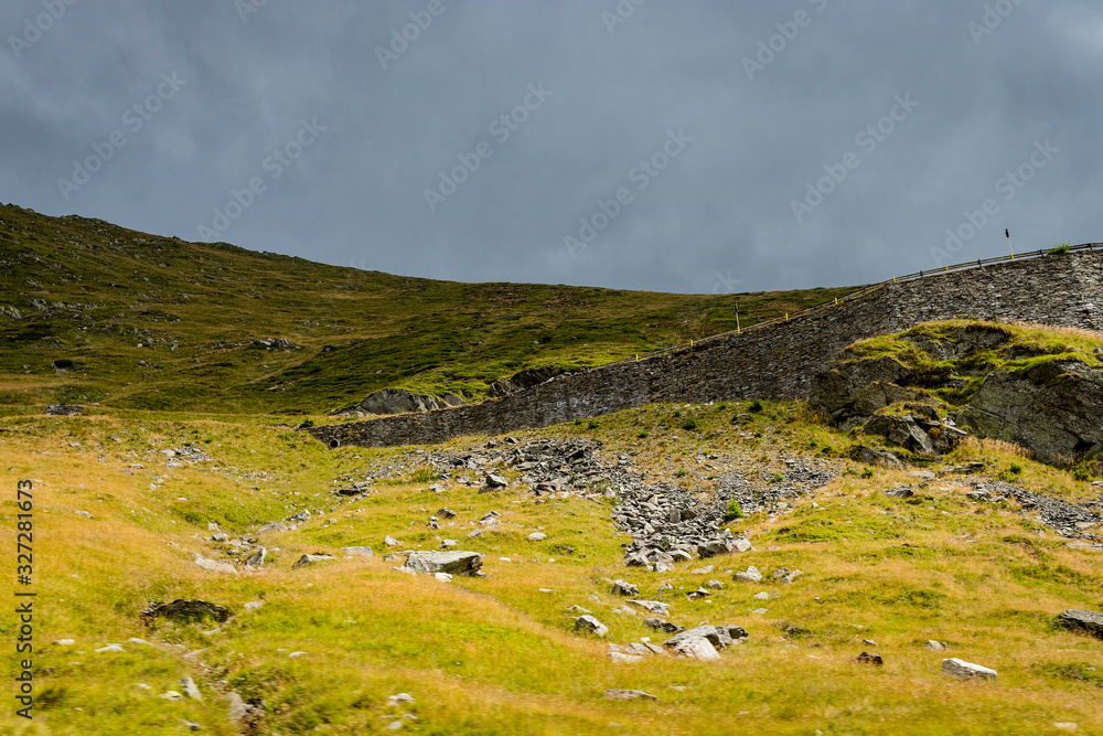 Upward view of a mountain road railing with fallen rocks in the foreground and dark sky in the background