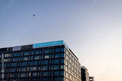Upward view of a large glass building at sunset with birds flying above