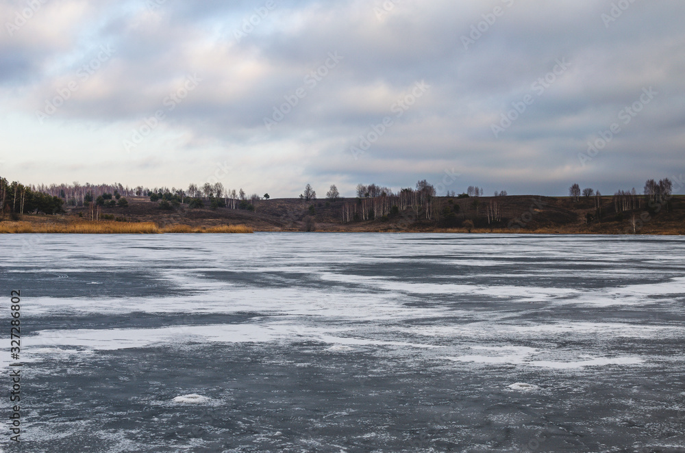 Scenery of a frozen lake and ravines in the background. On a cloudy day, fishermen stopped fishing on a frozen lake and went home