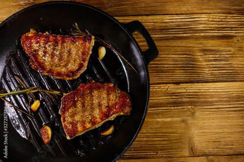Grilled pork steaks with rosemary, garlic and spices in cast iron grill frying pan on wooden table. Top view