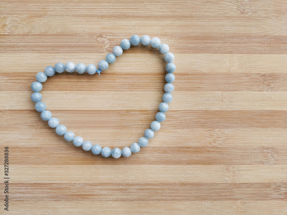 Aquamarine beads strand in a heart shape on wood background. Concept of love, kindness and valentine's day. Aquamarine beads strand in a heart shape on wood background. Concept of love, kindness and valentine's day.