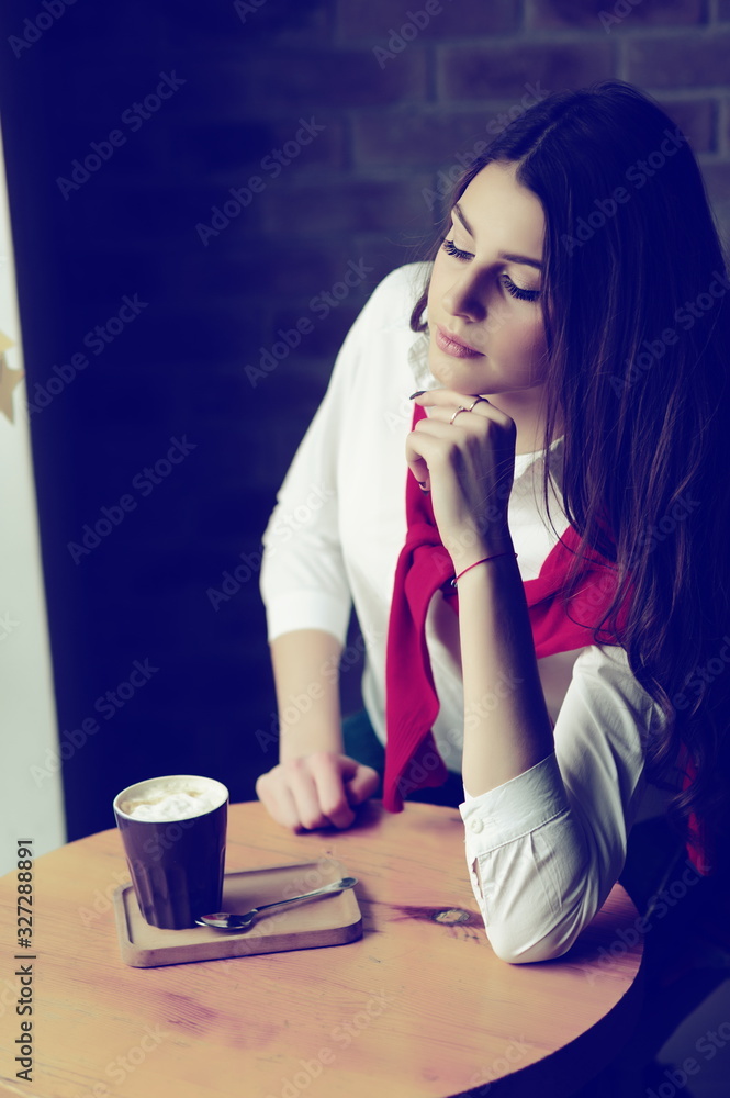 Girl at a table by the window in a cafe with a cup of coffee Girl at a table by the window in a cafe with a cup of coffee