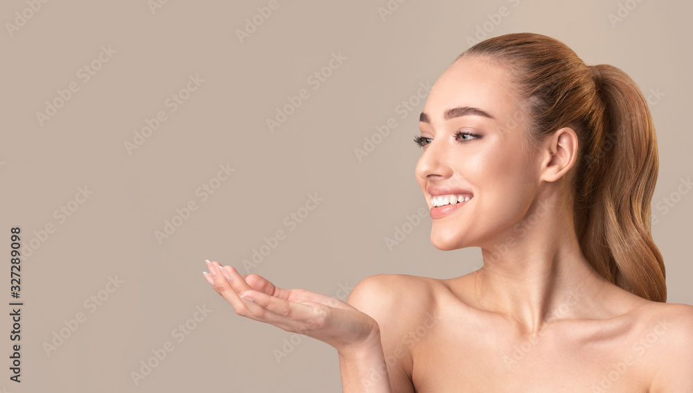 Woman Posing Holding Invisible Object On Hand Over Beige Background Woman Posing Holding Invisible Object On Hand Over Beige Background