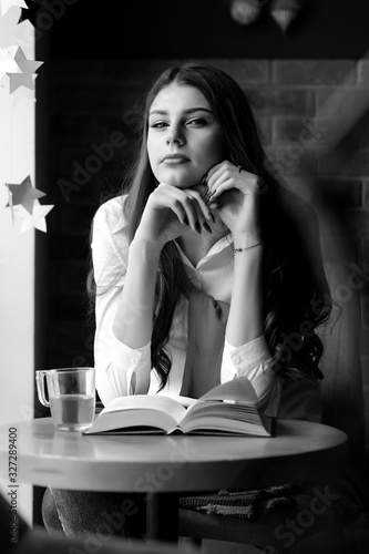 Girl at a table by the window in a cafe with a cup of tea and a book