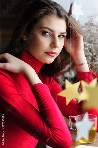Beautiful girl in a red sweater at the window in a cafe with a cup of tea and a book